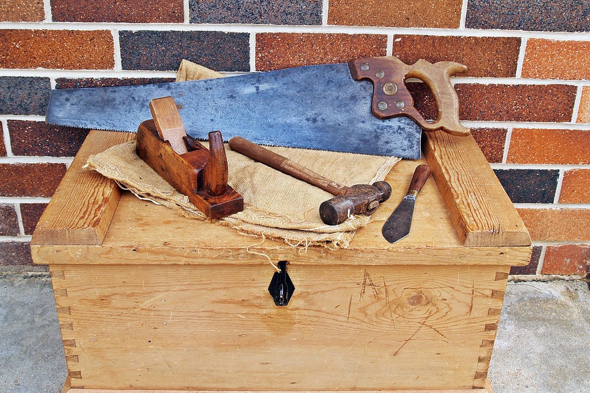 Hand tools resting on a wooden tool chest against a brick wall